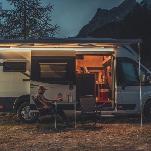 Caucasian Men in His 40s Working Online While on Vacation in Mountain Region. Remote Work on Laptop While Camping in a Wild. Camper Van as Mobile Office Theme.